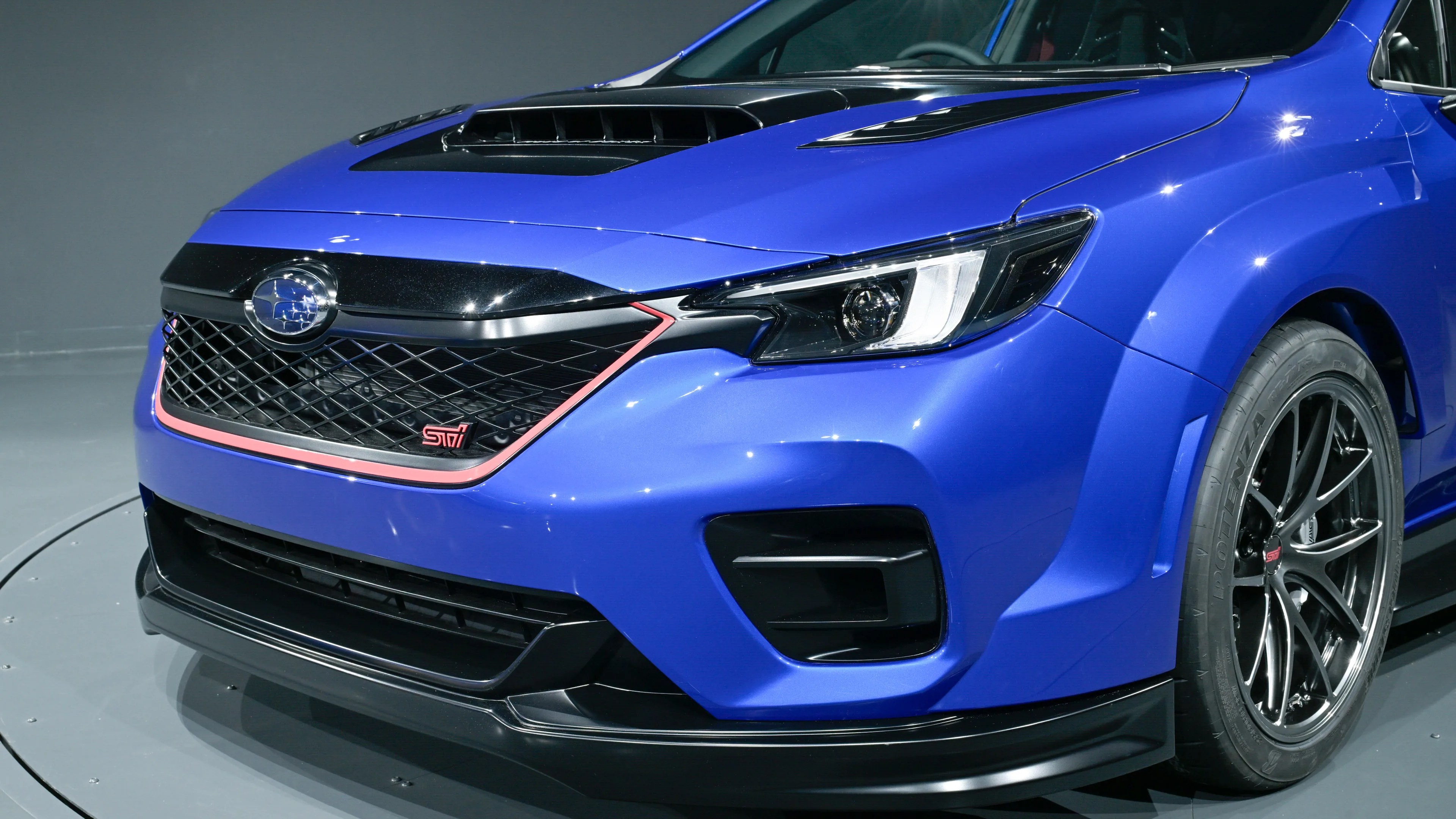Front view of a blue Subaru STI car with black grille, hood scoop, and black alloy wheels.