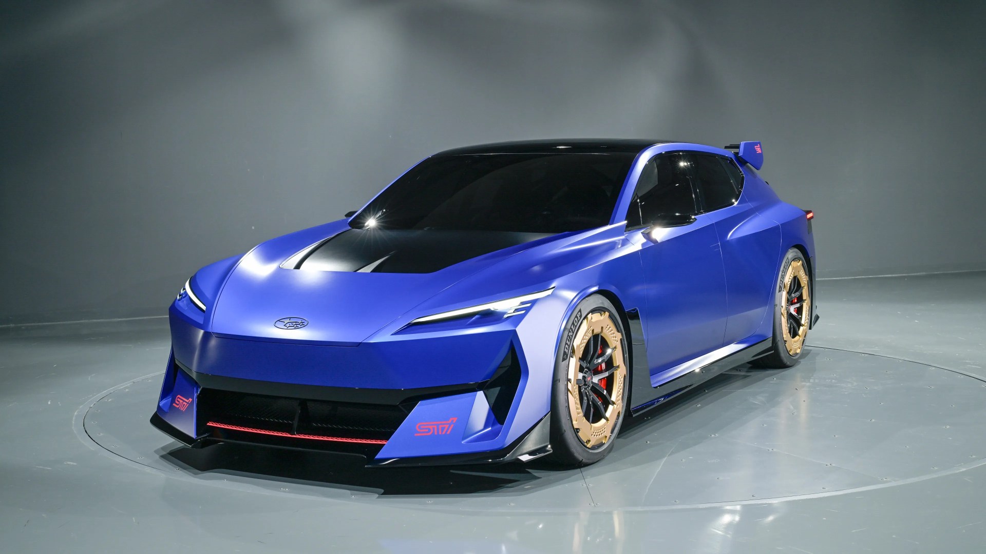 Blue Subaru sports car with black hood, gold wheels, and red STI logos in a gray studio.