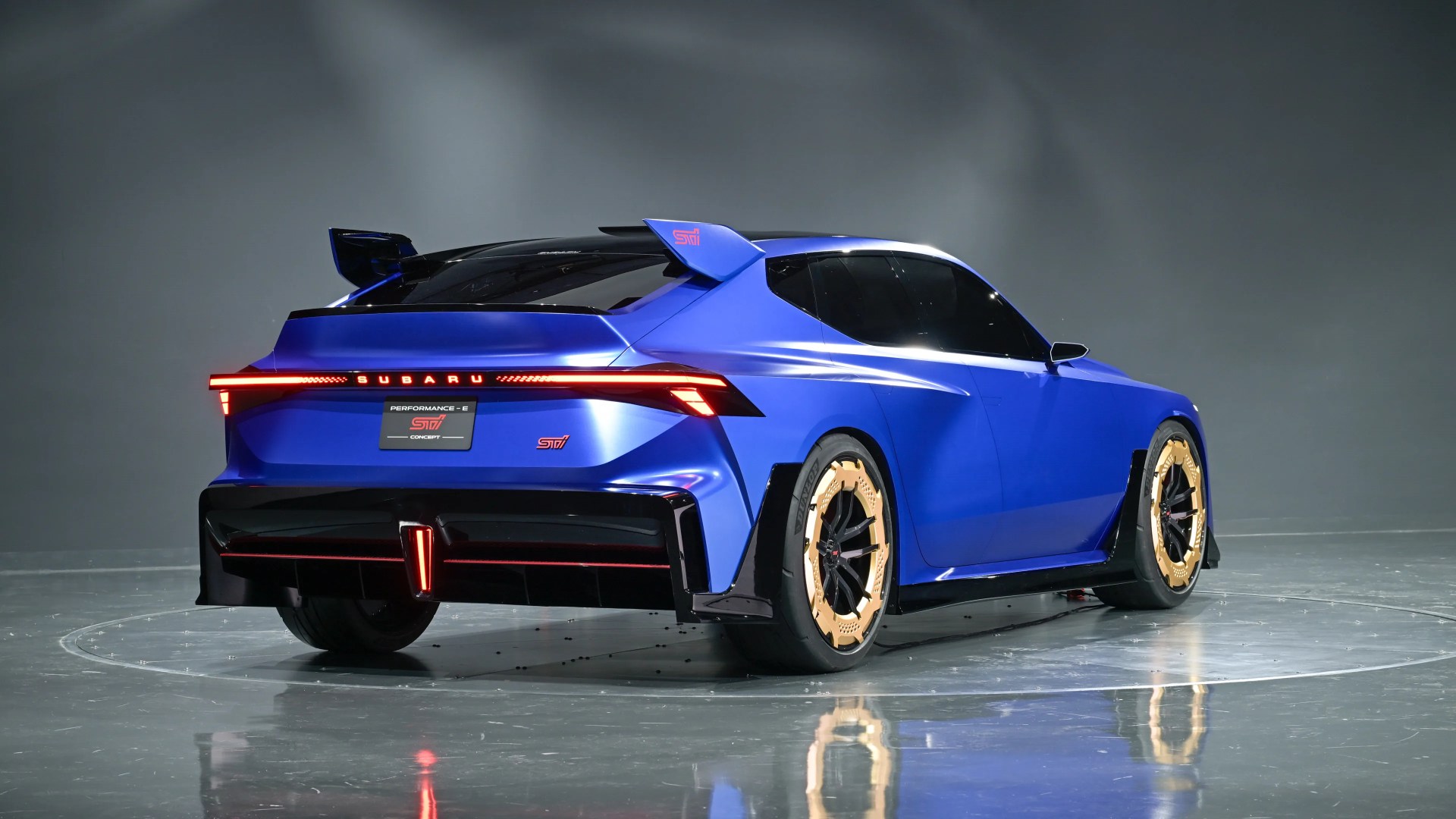 Blue Subaru Performance-E STI concept car with gold-accented wheels and rear spoiler in a studio.