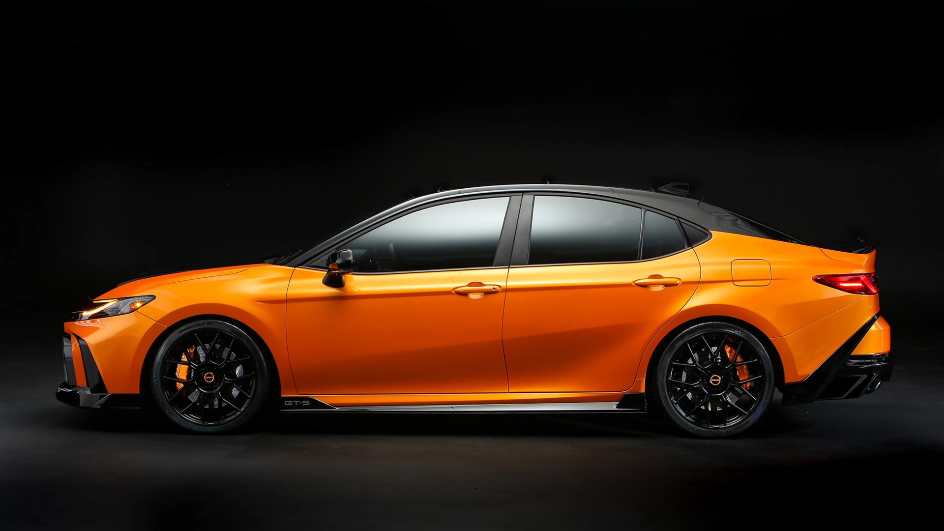 Orange and black sporty sedan with black wheels and tinted windows on a black background.