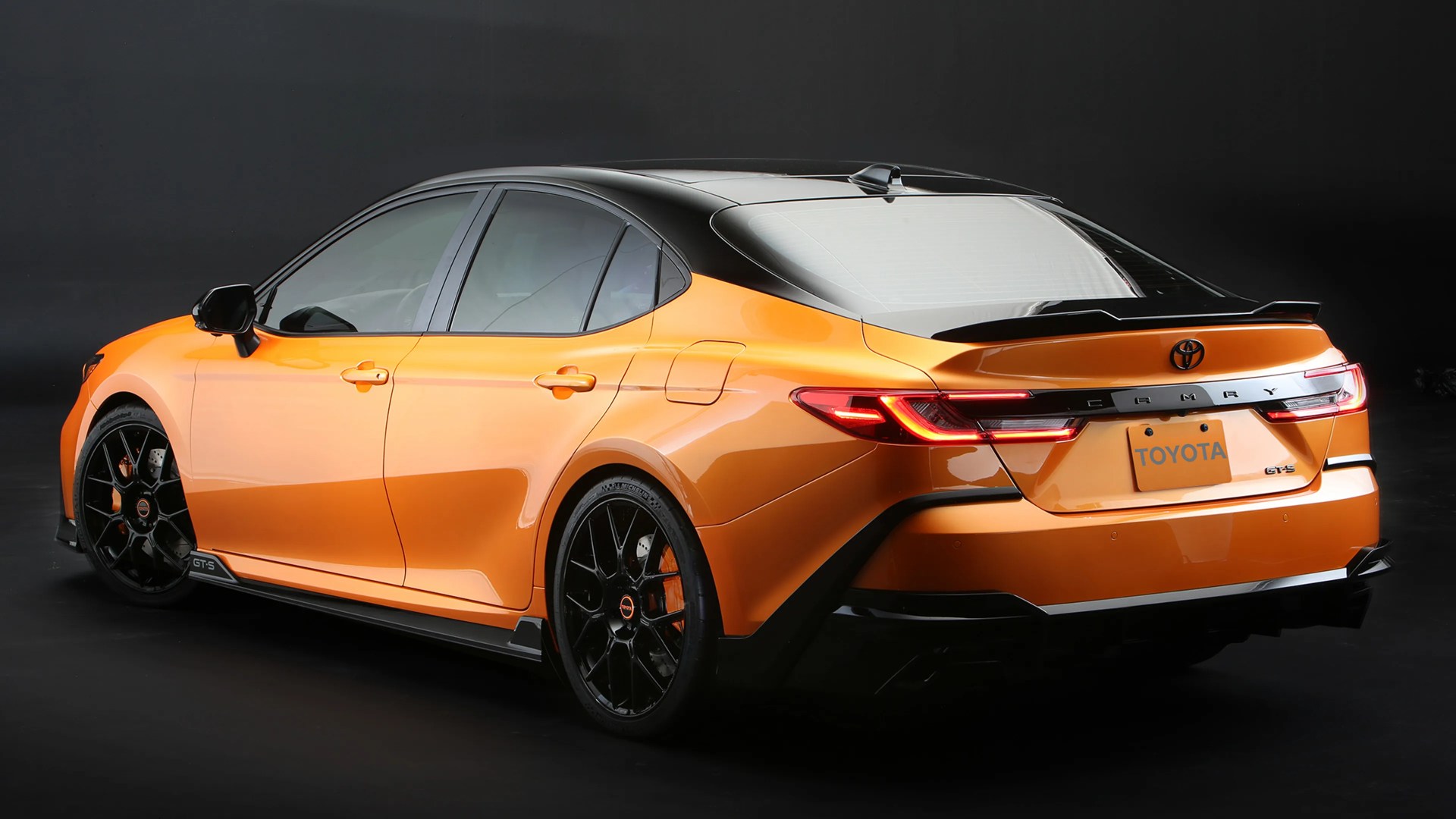 Orange and black Toyota Camry GTS sedan with black alloy wheels on a black background.