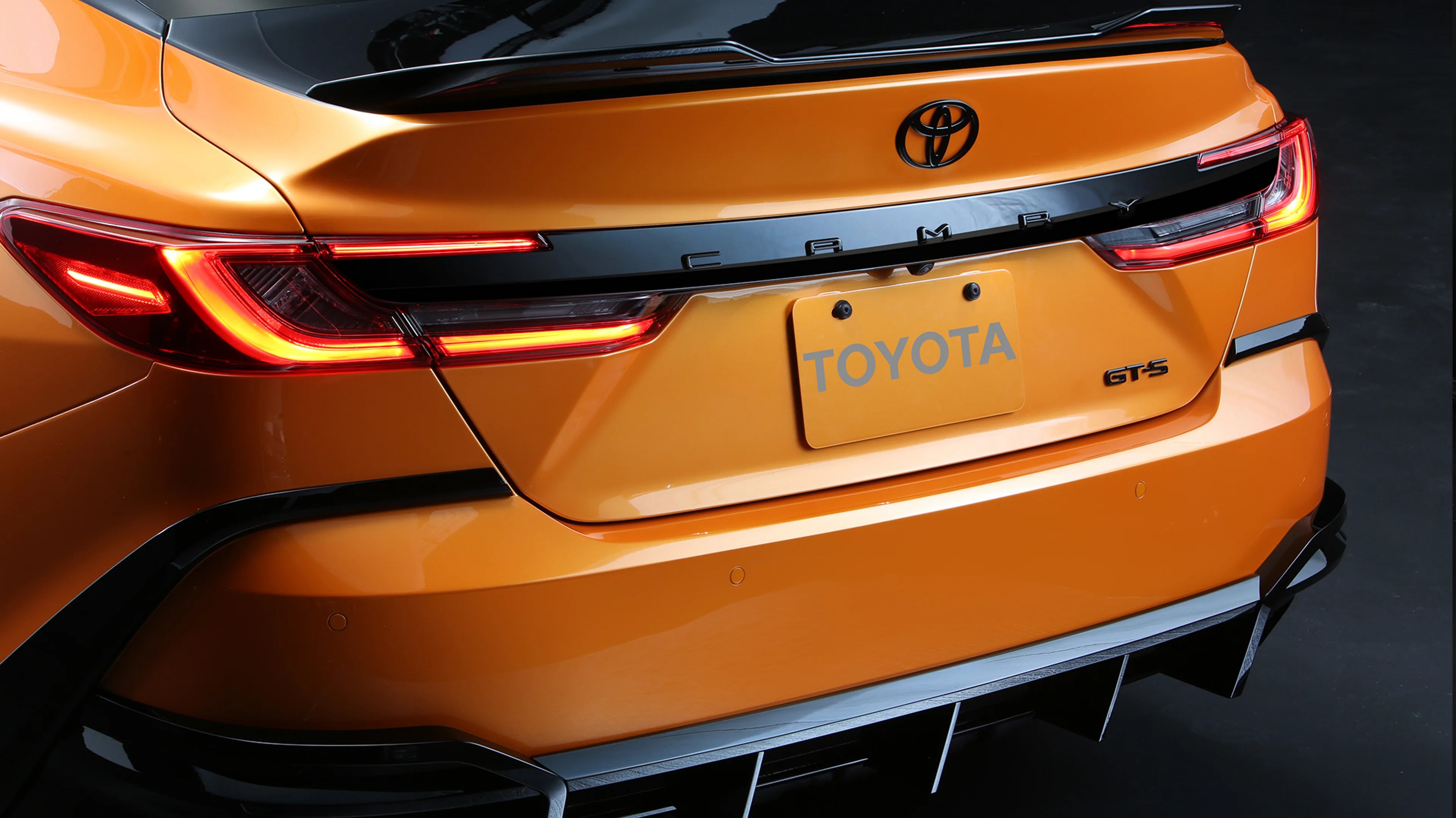 Rear view of an orange Toyota Camry GTS with illuminated taillights and black trim accents.