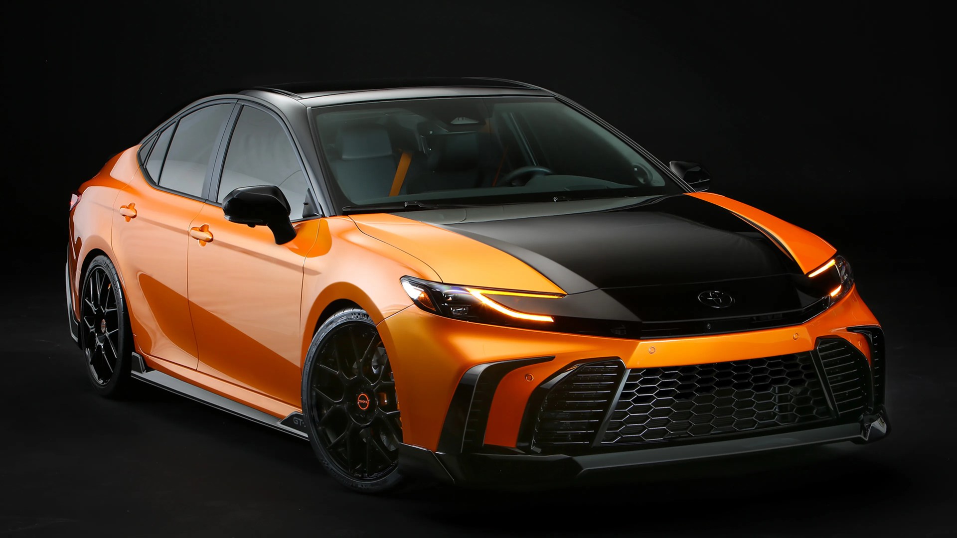 Orange and black Toyota sedan with aggressive front grille and sleek LED headlights on black background.