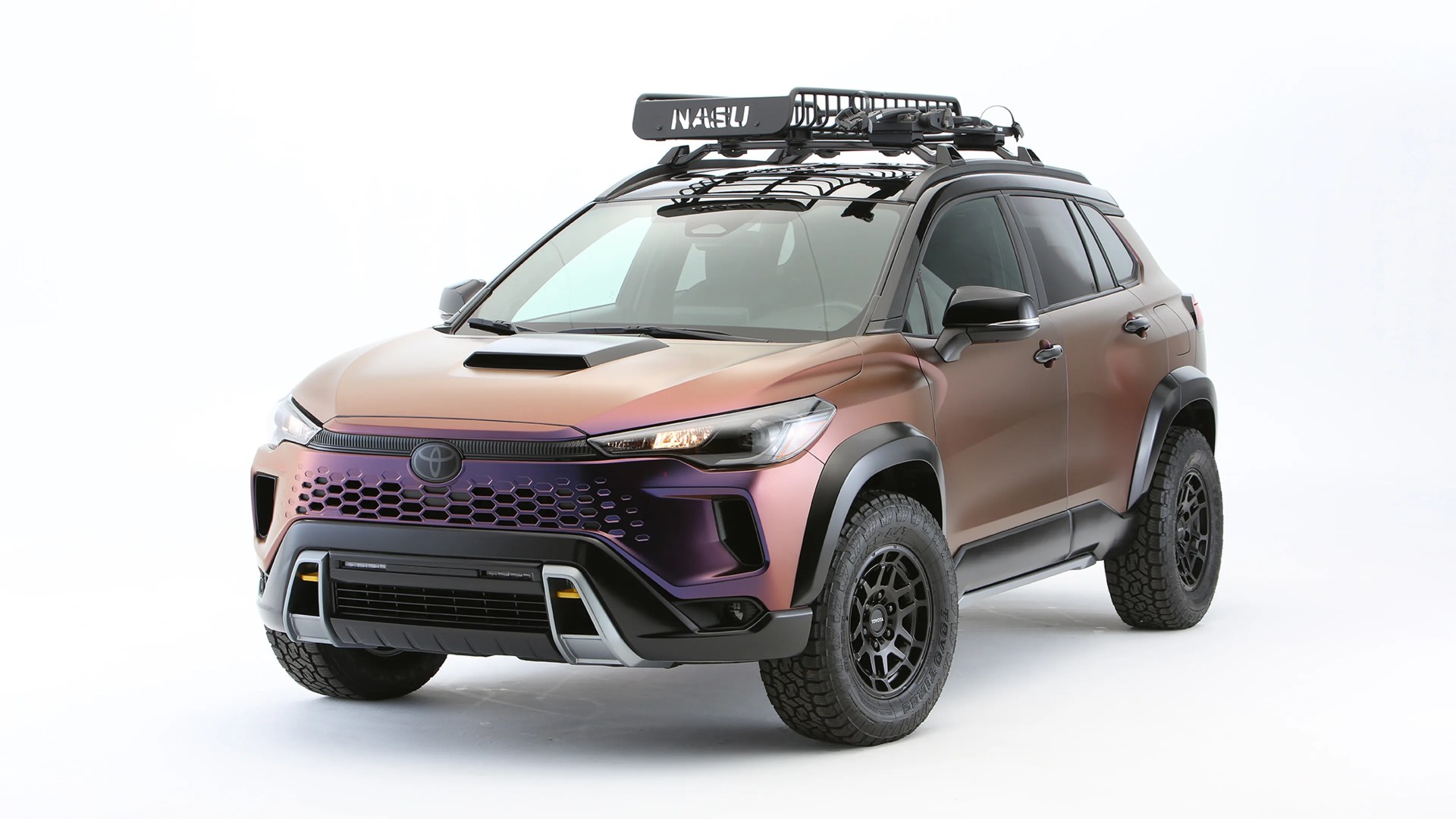 Matte chameleon-colored Toyota SUV with black roof rack and off-road tires on a white background.