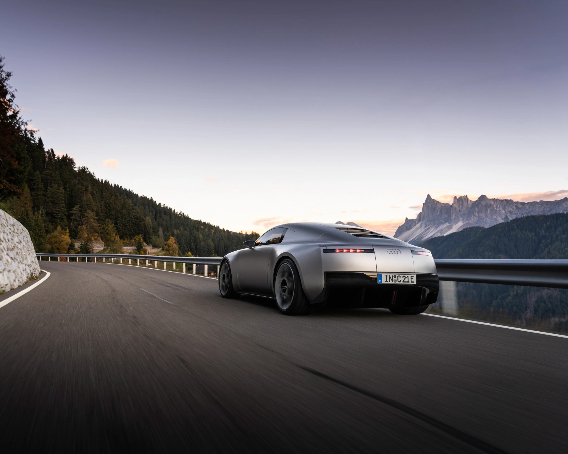 Matte silver Audi concept car driving on a winding mountain road at sunset.