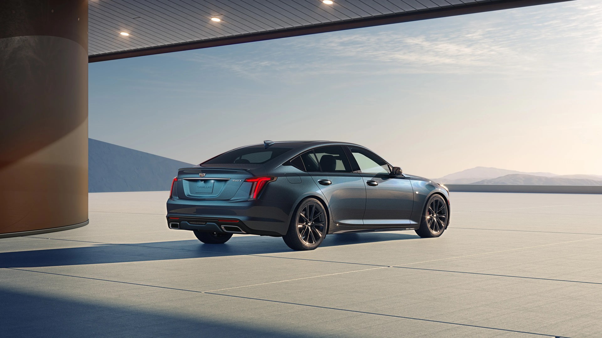 Dark gray Cadillac CT5 sedan parked on a concrete surface under a modern canopy with mountains in the background.