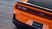 Rear view of an orange Dodge car showing taillights, black spoiler, and a black and white Dodge license plate.