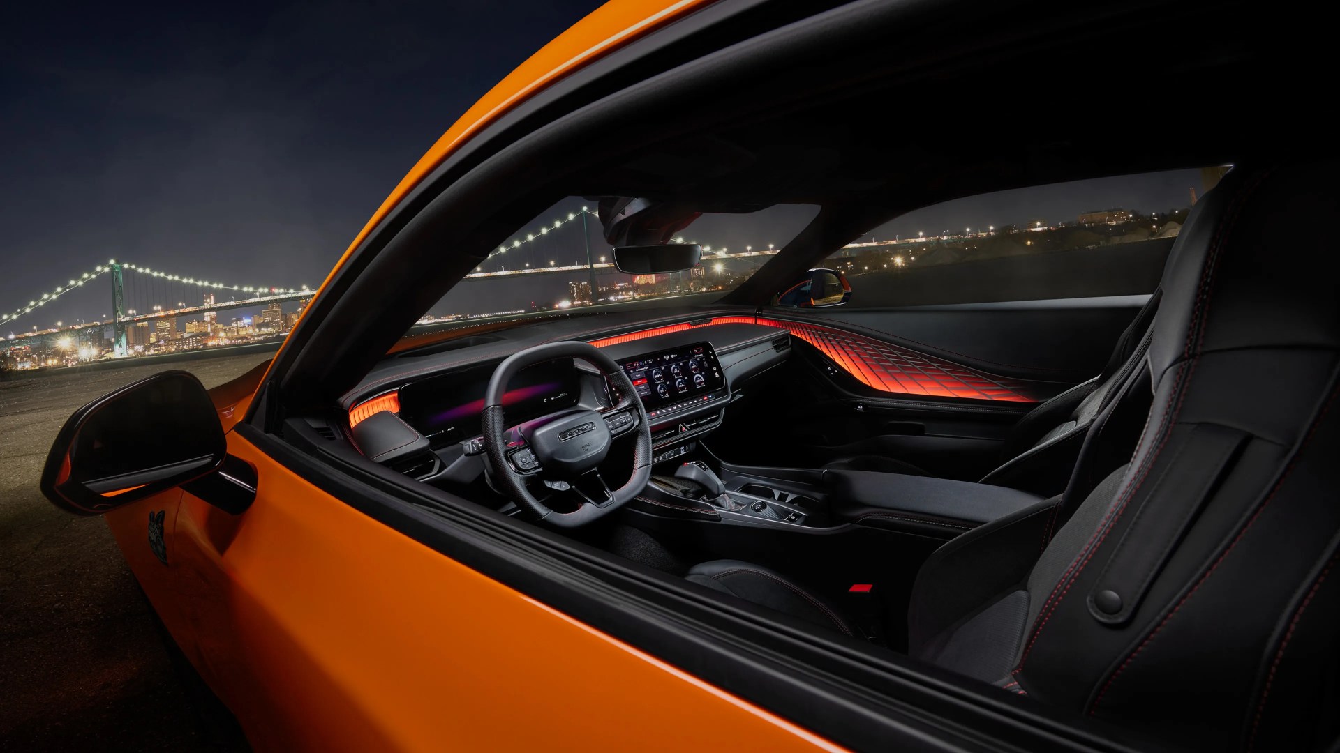 Interior of an orange sports car at night with illuminated red ambient lighting on the dashboard and black leather seats.