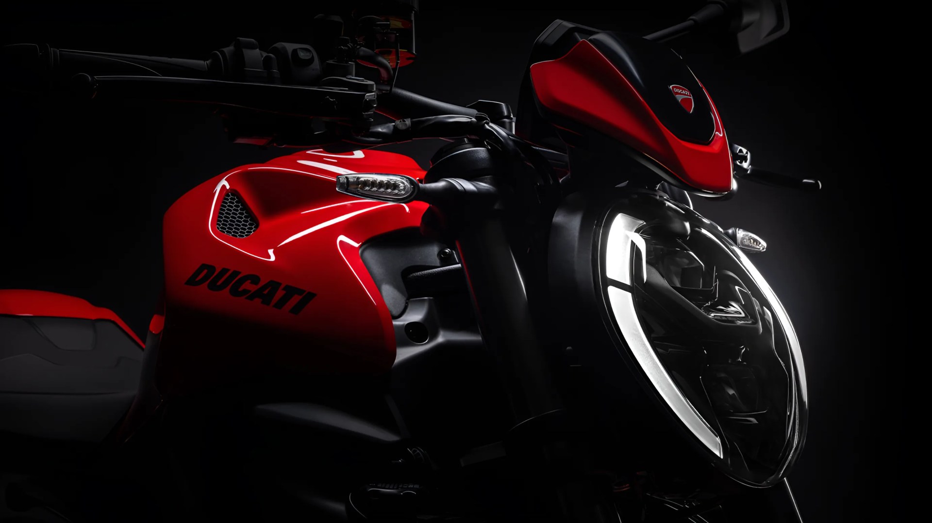 Close-up of a red Ducati motorcycle front with illuminated headlight and visible logo on the fuel tank.
