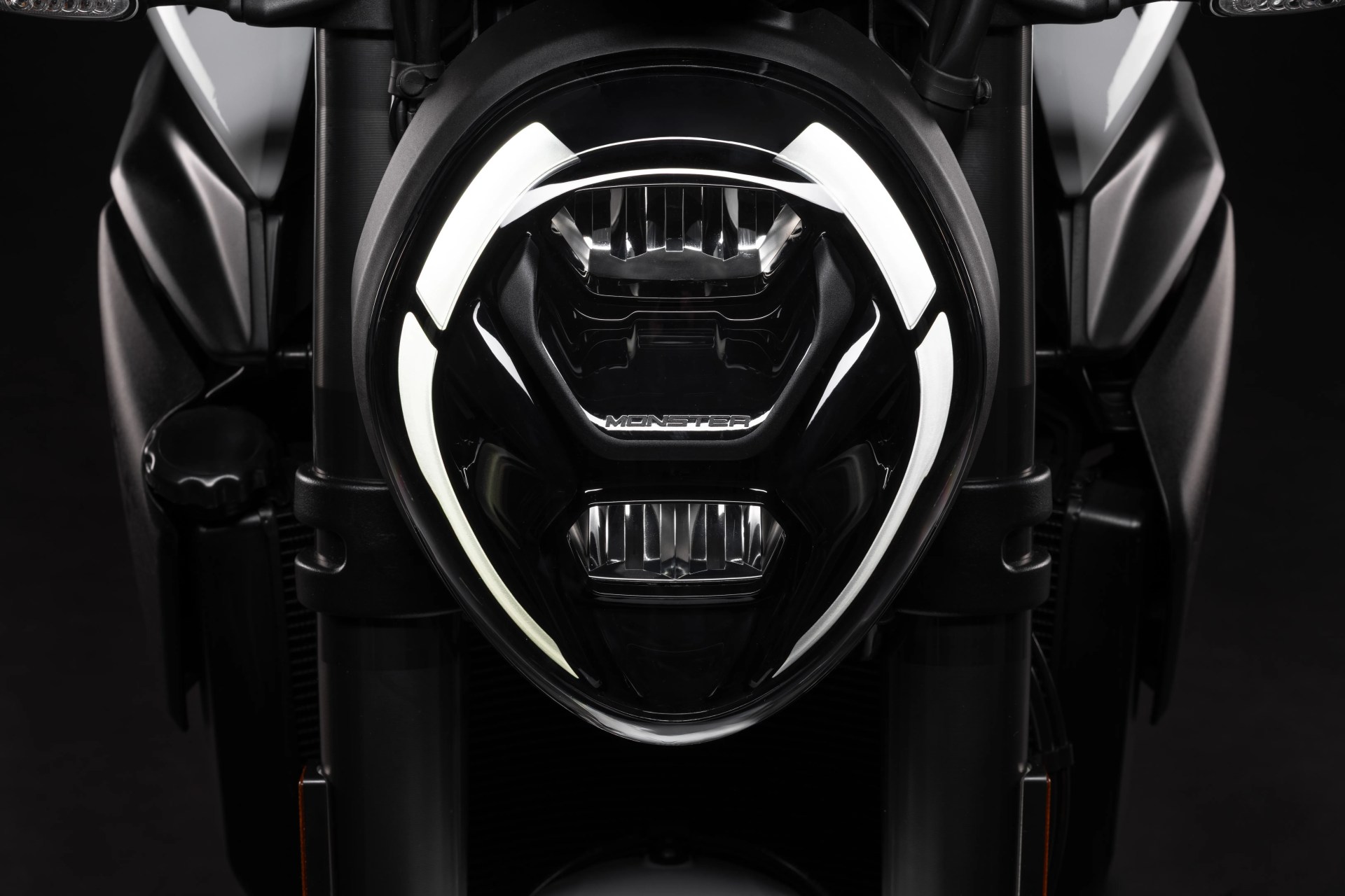Close-up of a black motorcycle headlight with white LED accents and the word "MONSTER" on the lens.
