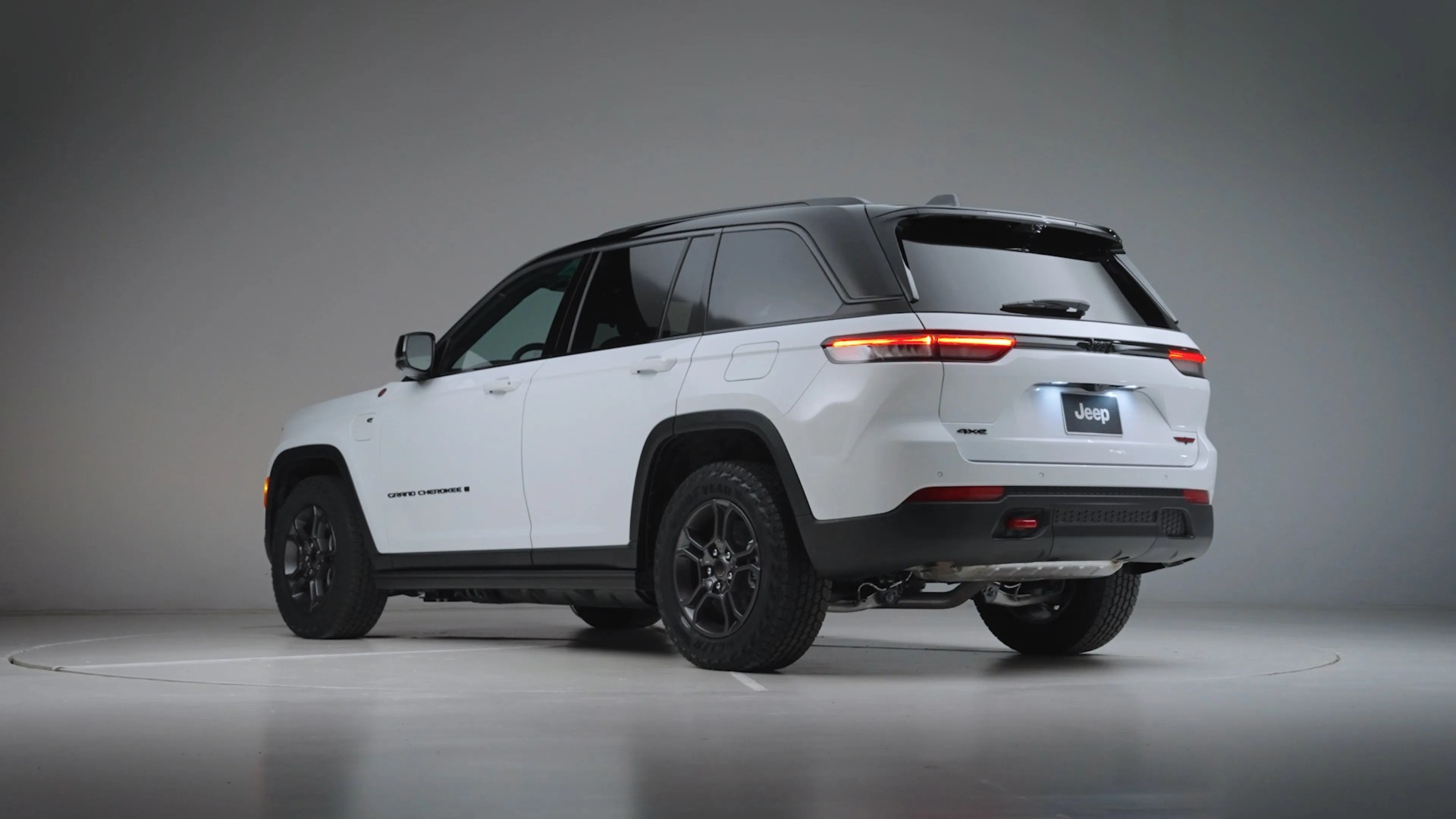 White Jeep Grand Cherokee 4xe SUV with black roof and tinted windows in a studio setting.