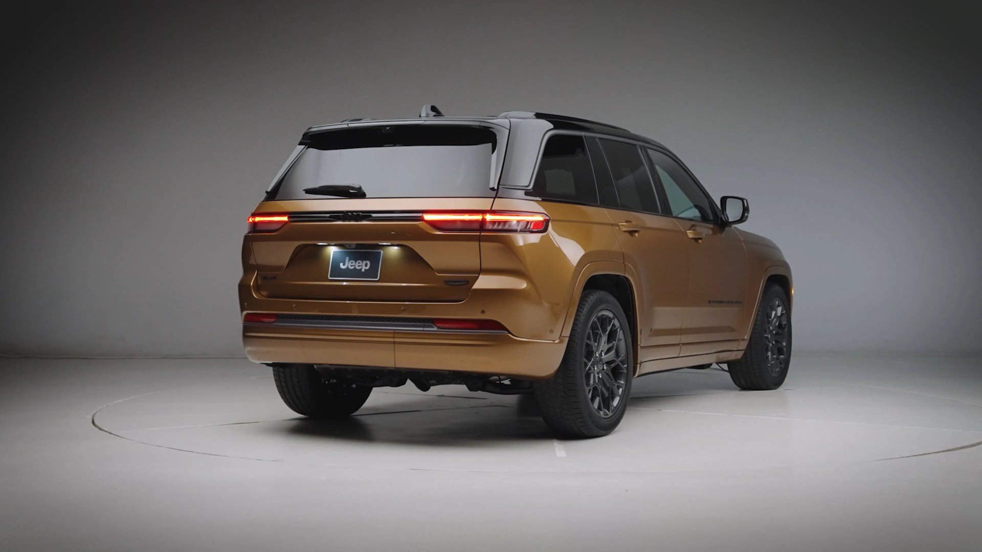 Bronze Jeep SUV with black roof and tinted rear windows in a studio setting.