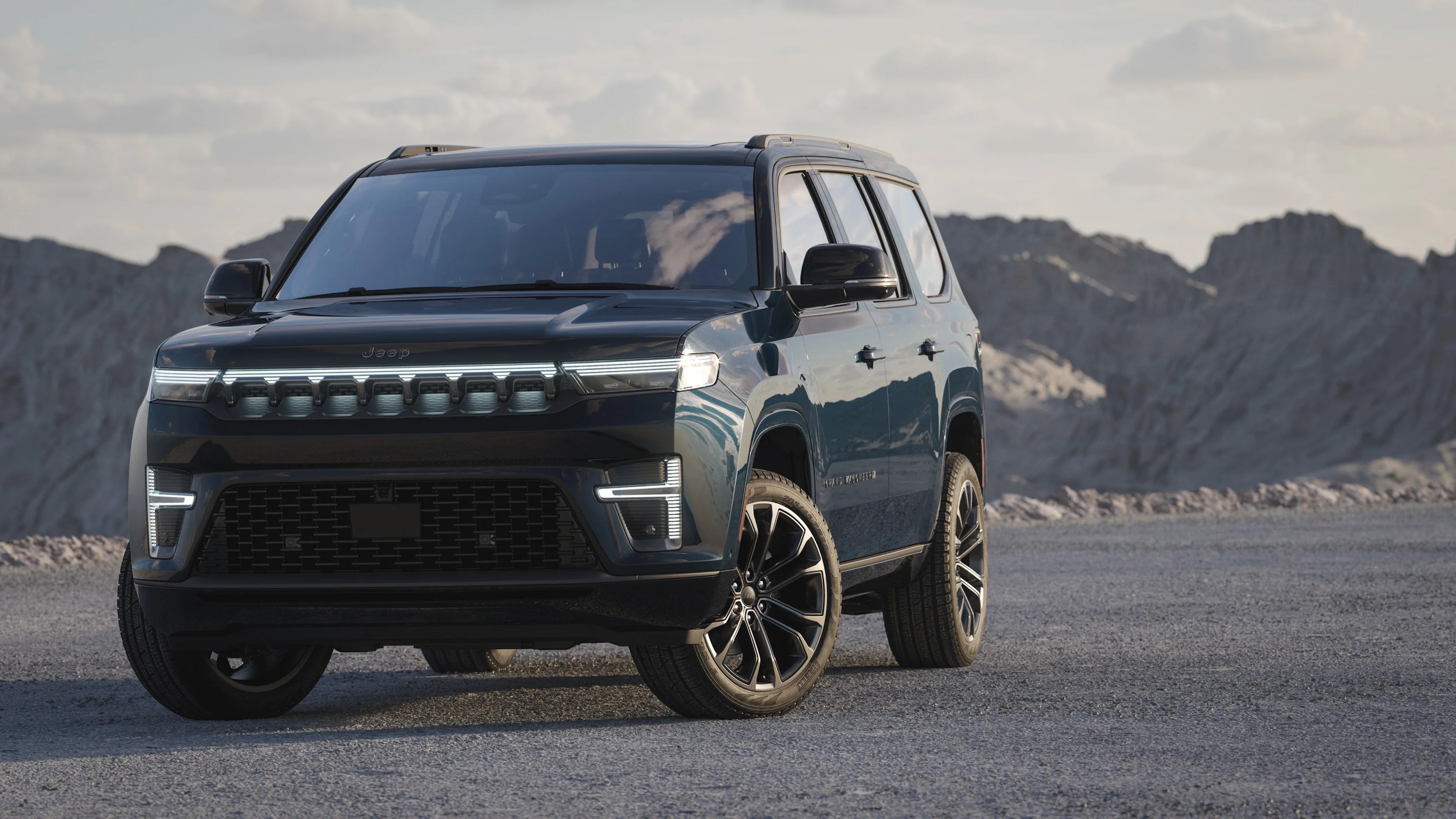 Dark blue Jeep SUV with LED headlights parked on a gravel surface with rocky hills in the background.