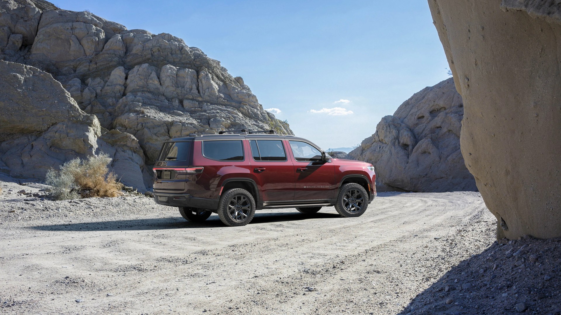 Maroon SUV with black roof and wheels parked on a dirt road surrounded by rocky terrain.