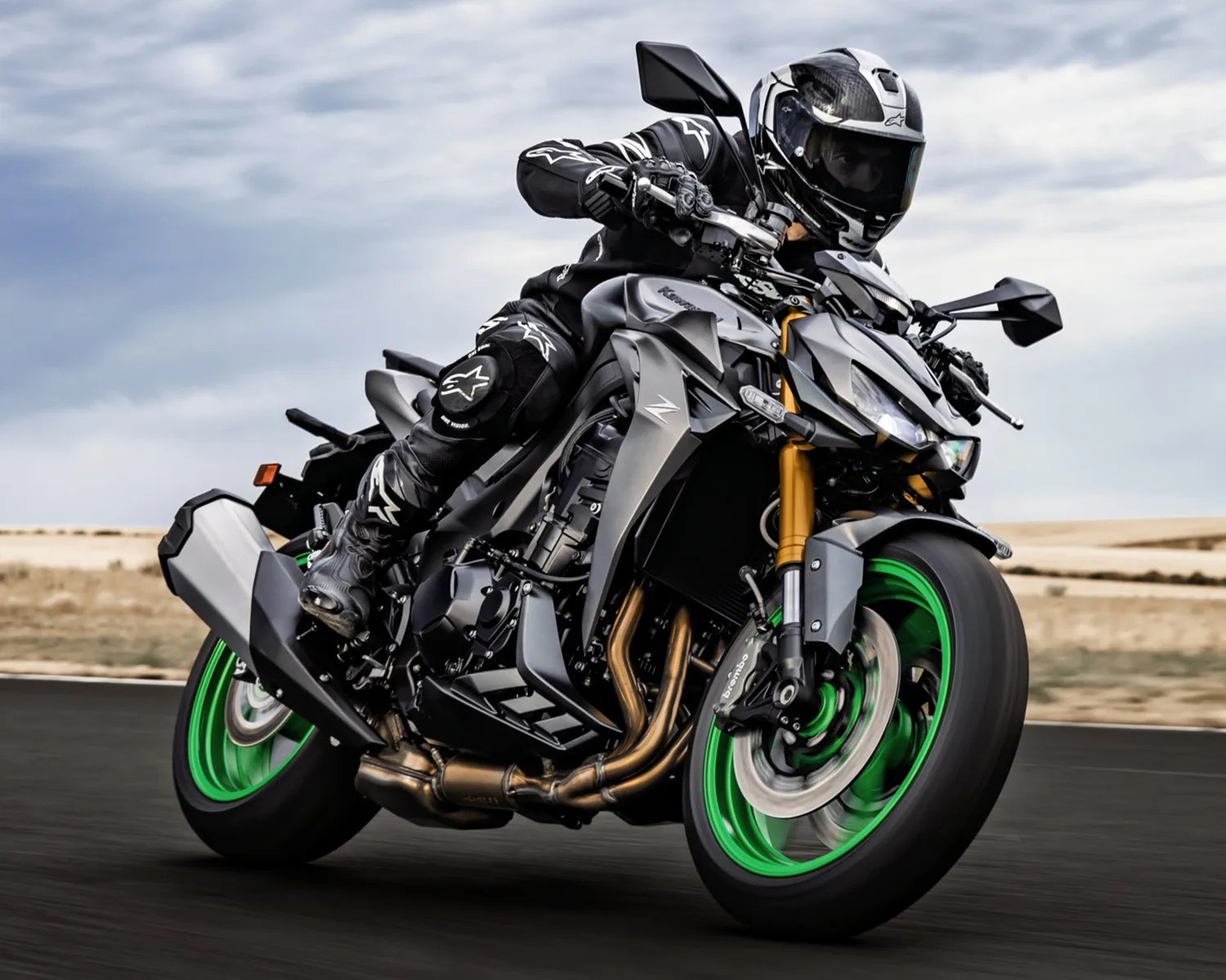 Black and gray Kawasaki motorcycle with green rims ridden on a road by a person in black gear and helmet.