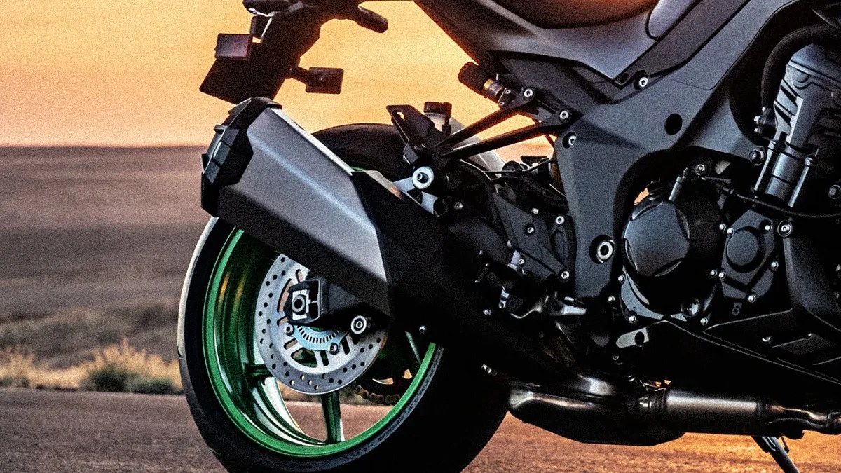 Close-up of a motorcycle's rear wheel with a green rim, black exhaust, and visible engine parts at sunset.