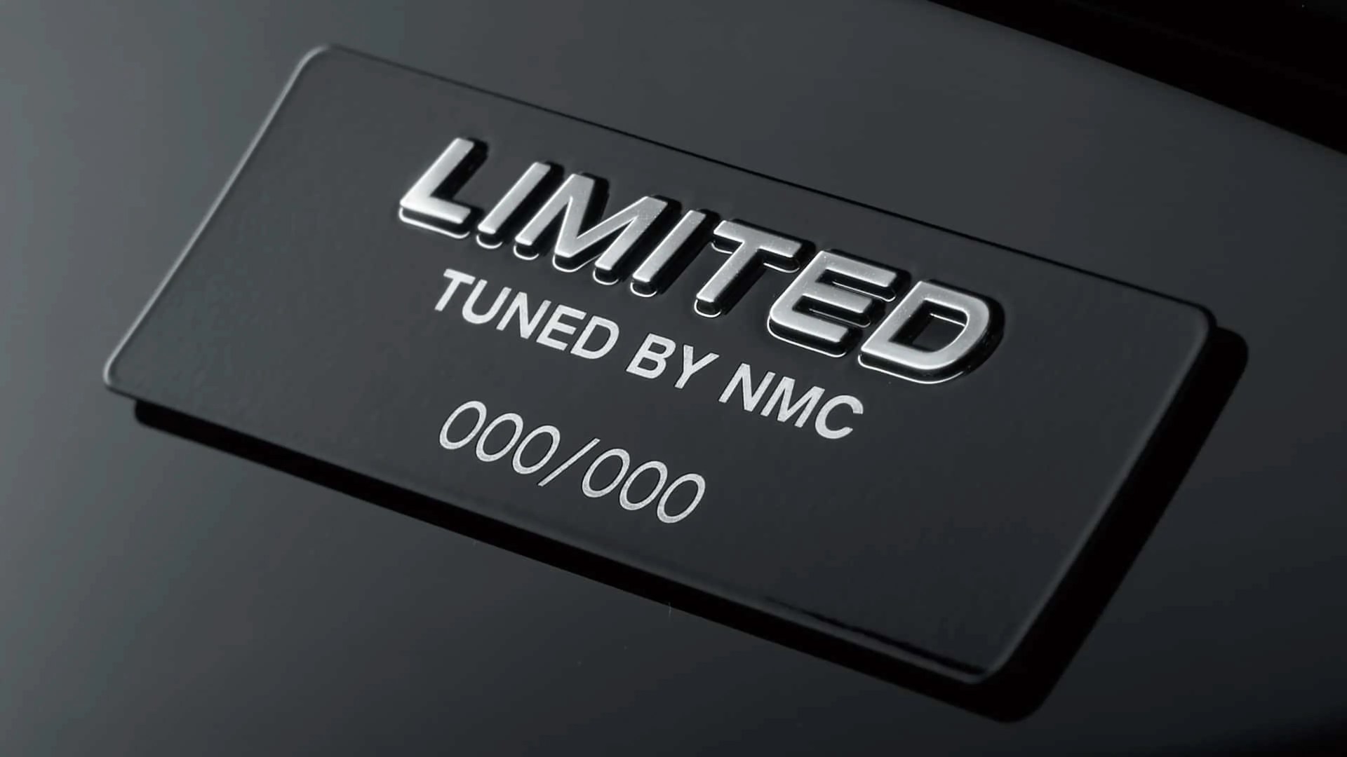 Black plaque with raised silver text "LIMITED" and printed text "TUNED BY NMC 000/000" on a glossy black surface.
