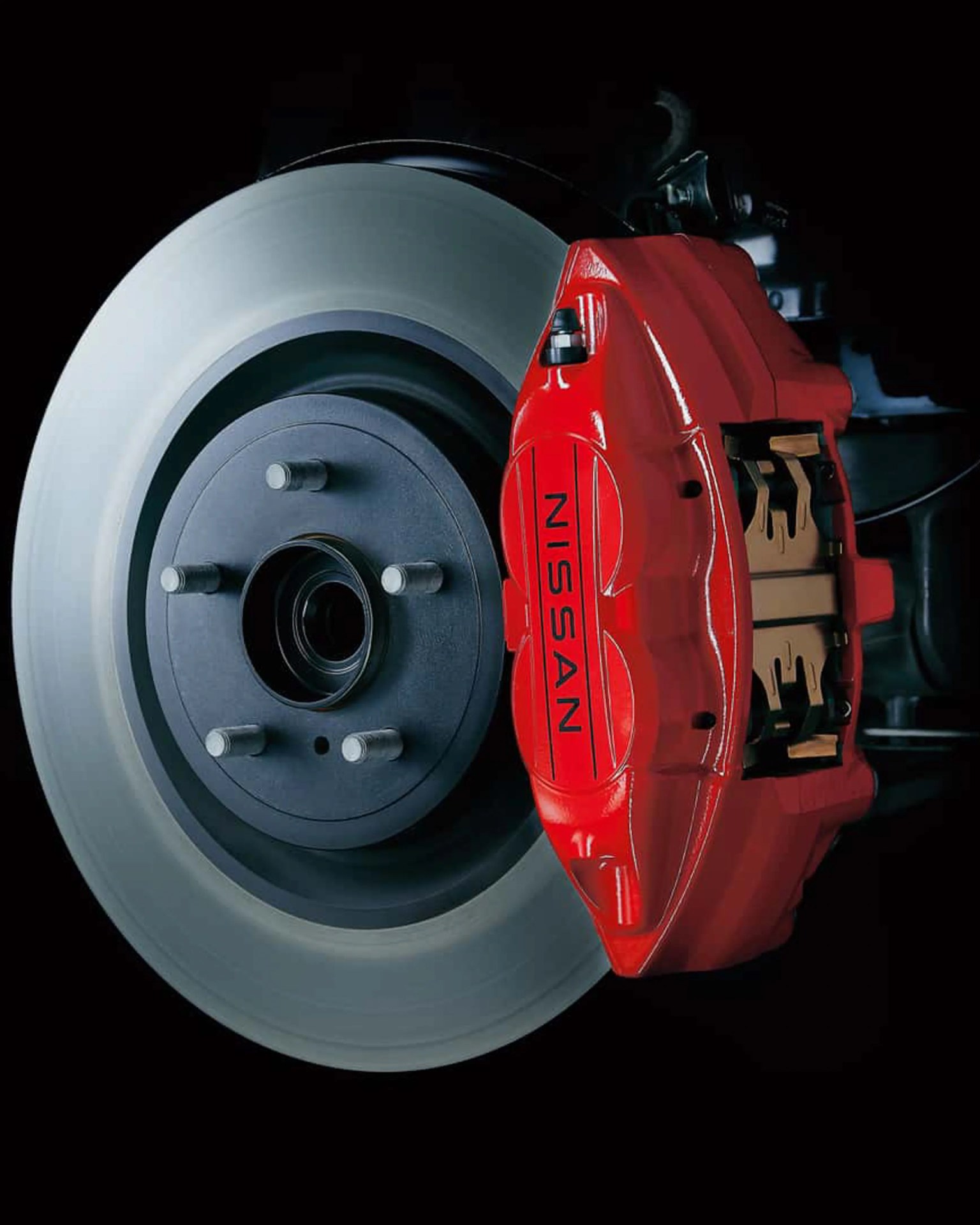 Red Nissan brake caliper mounted on a silver brake disc against a black background.