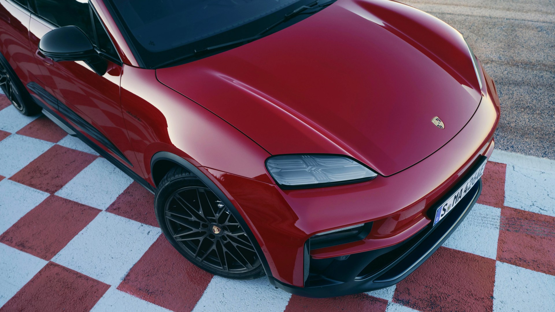 Red Porsche Macan with black wheels parked on a red and white checkered surface.