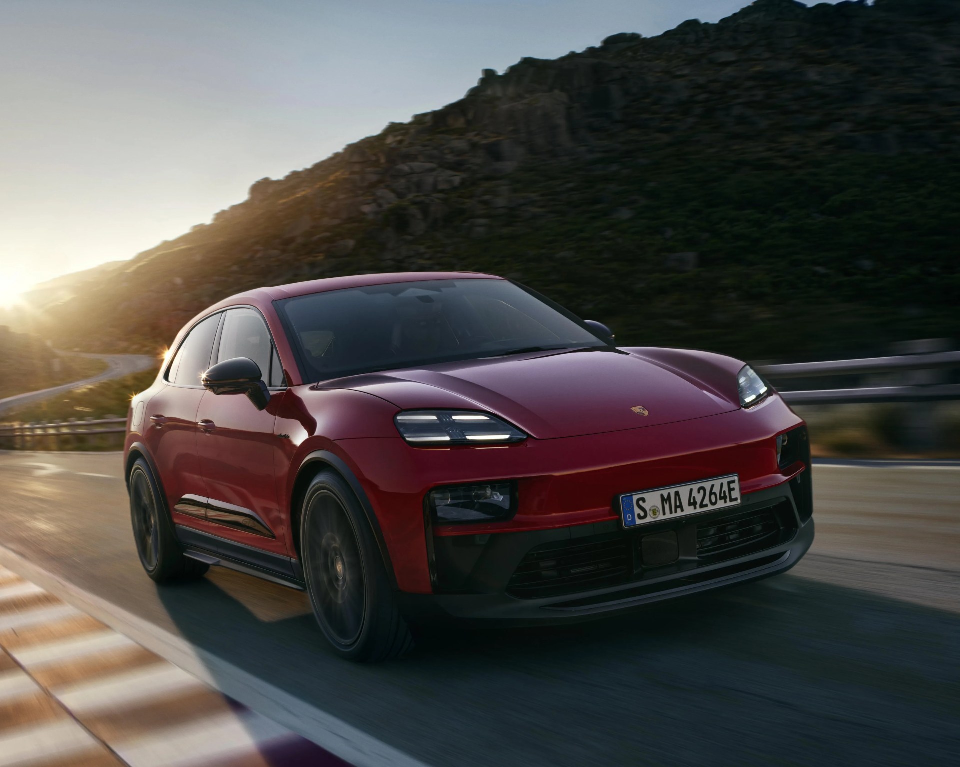 Red Porsche Macan electric SUV driving on a mountain road at sunset.