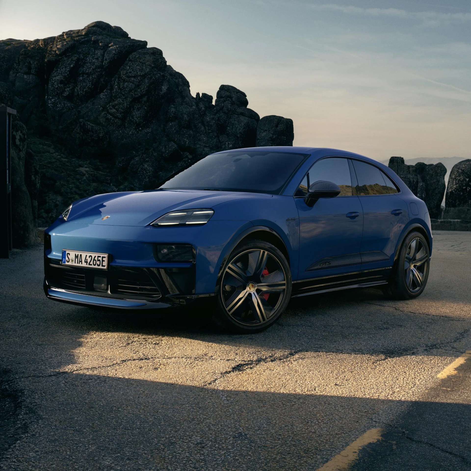 Blue Porsche electric SUV with black trim and large alloy wheels parked on a paved area near rocky terrain.