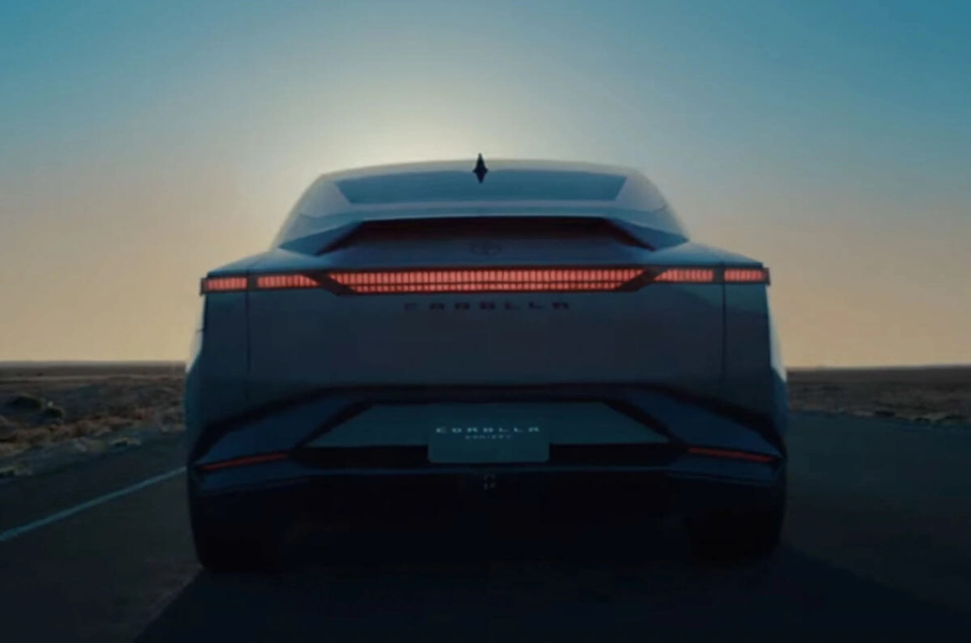 Rear view of a dark-colored Hyundai Ioniq 6 electric car with illuminated taillights on a road at sunset.