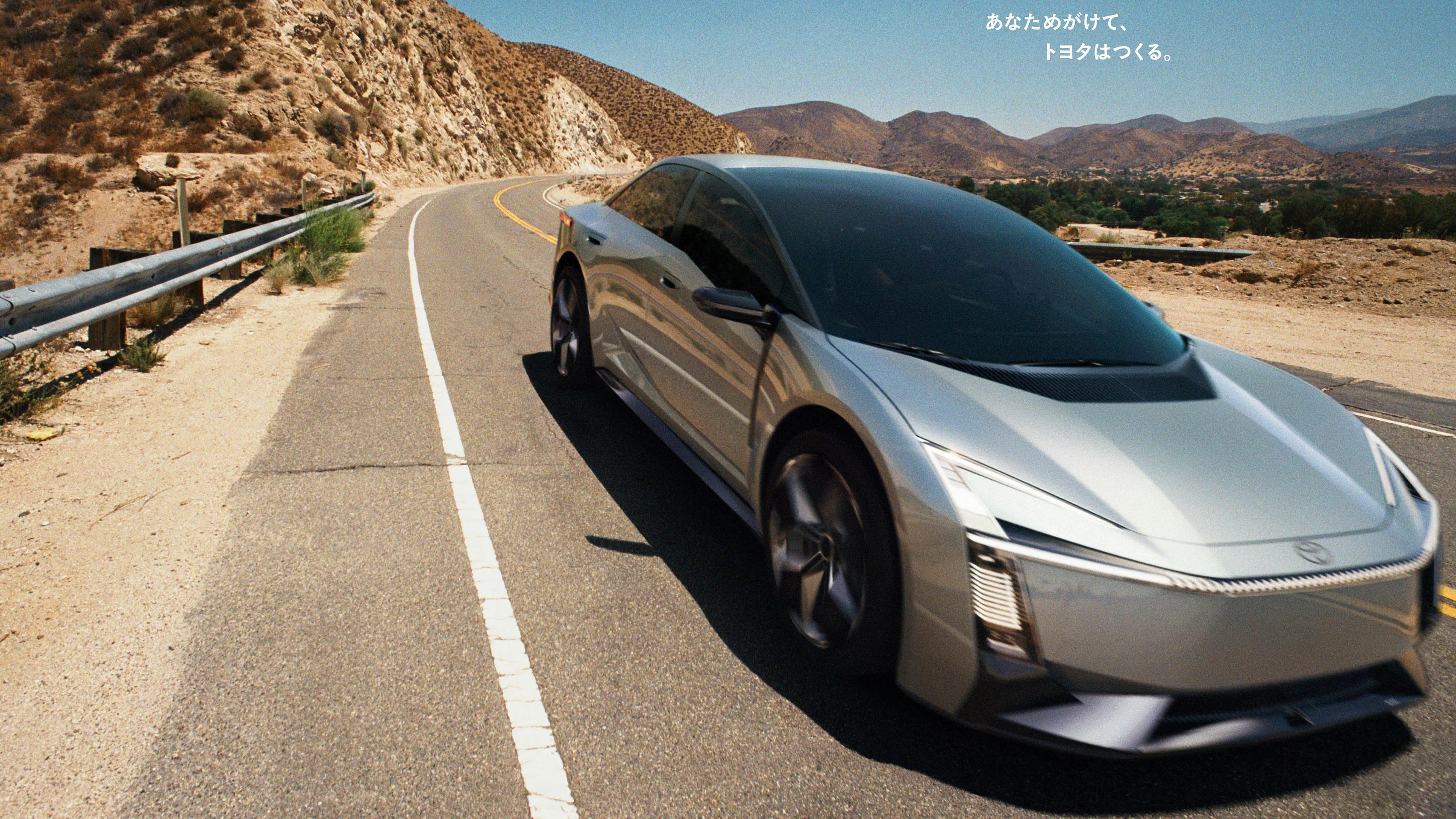 Silver futuristic electric car with tinted windows driving on a mountain road with dry hills in the background.