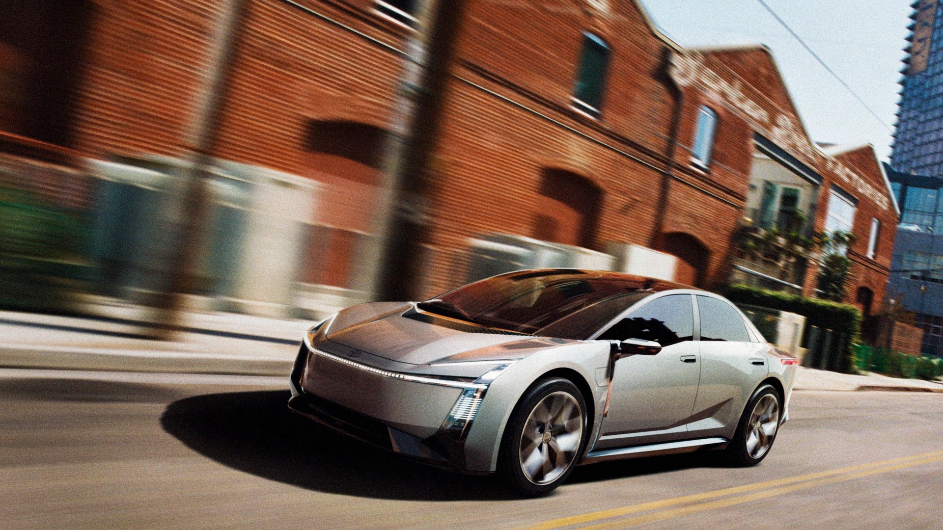 Silver electric sedan with sleek design driving on city street with brick buildings in background.