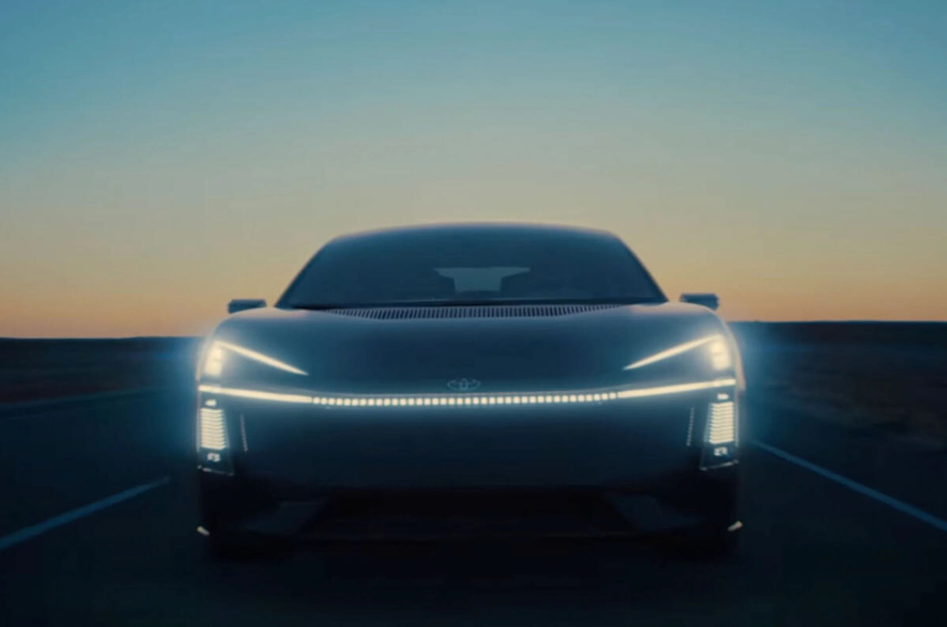 Front view of a sleek black electric car with illuminated LED headlights and light strip at dusk on a road.