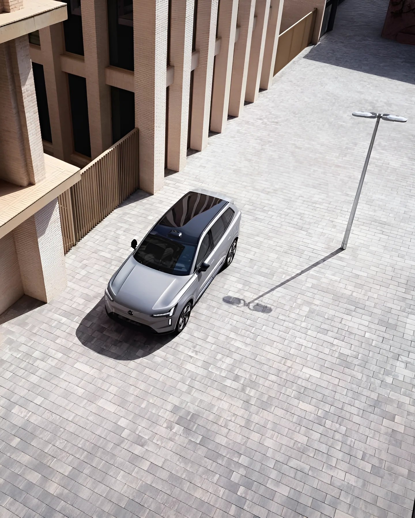 Silver electric SUV with black roof parked on light gray tiled pavement near beige building columns.