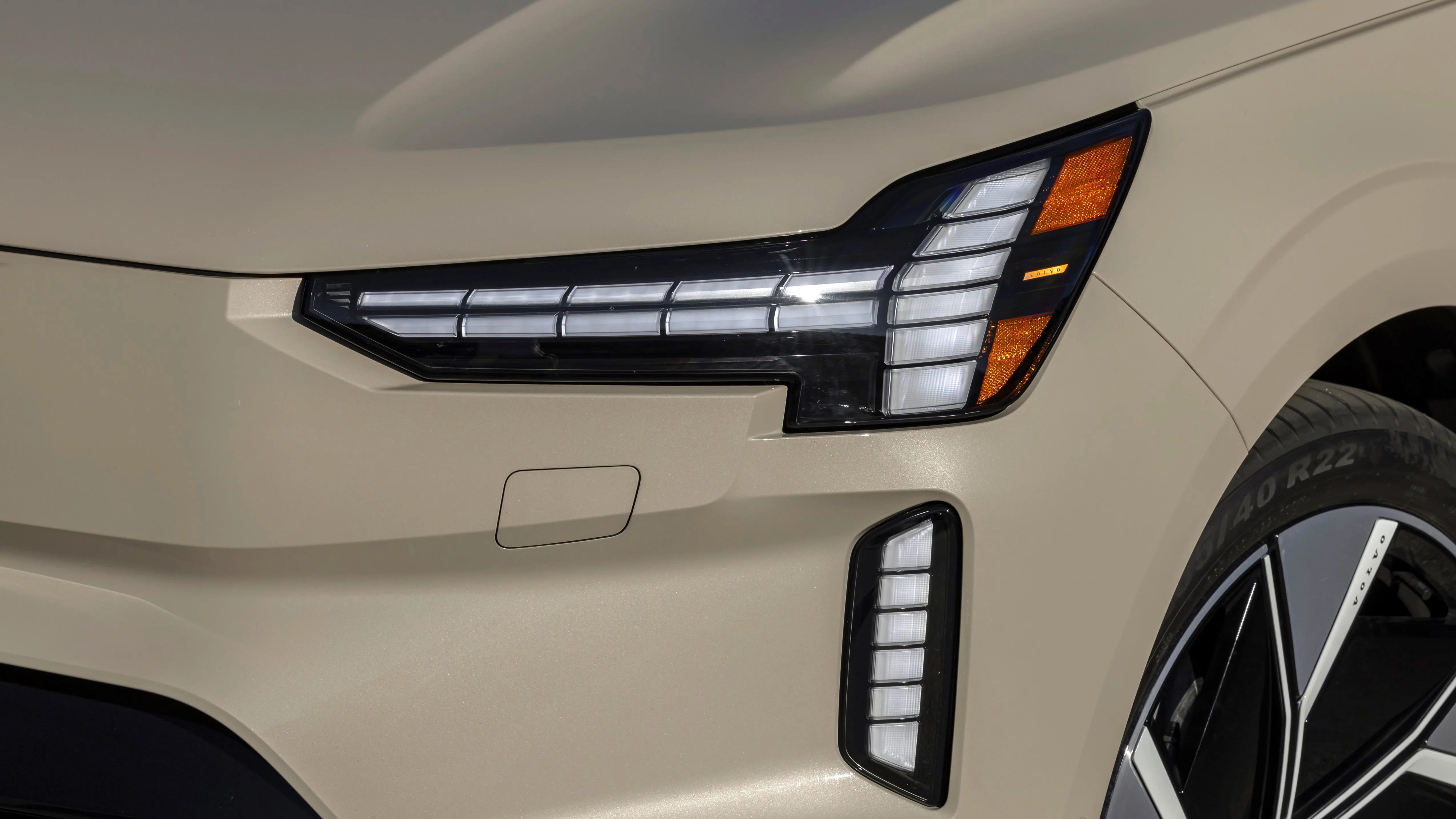 Close-up of beige car front showing angular LED headlight, vertical LED daytime running light, and part of a black and silver wheel.