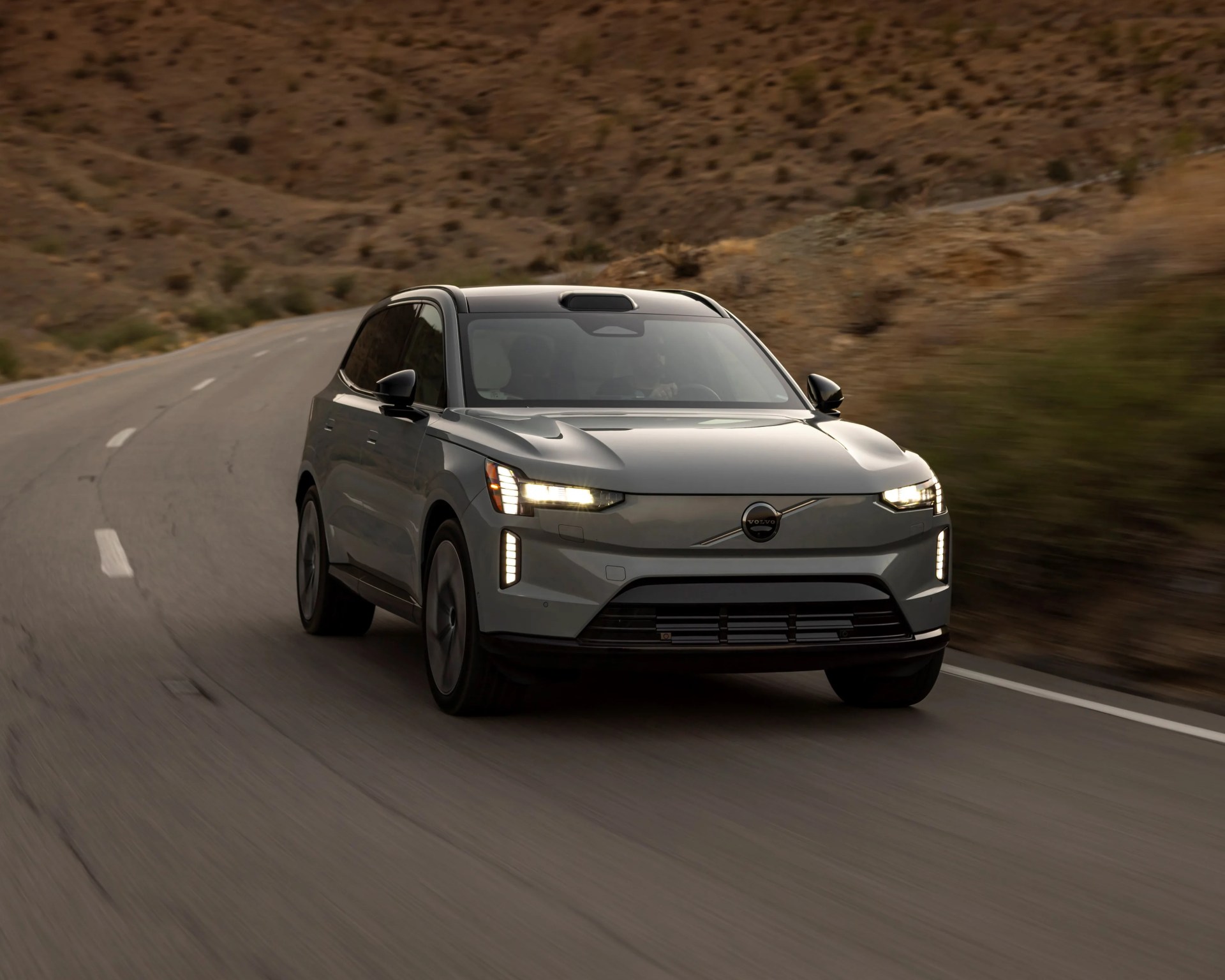 Gray Volvo SUV with LED headlights driving on a winding desert road.