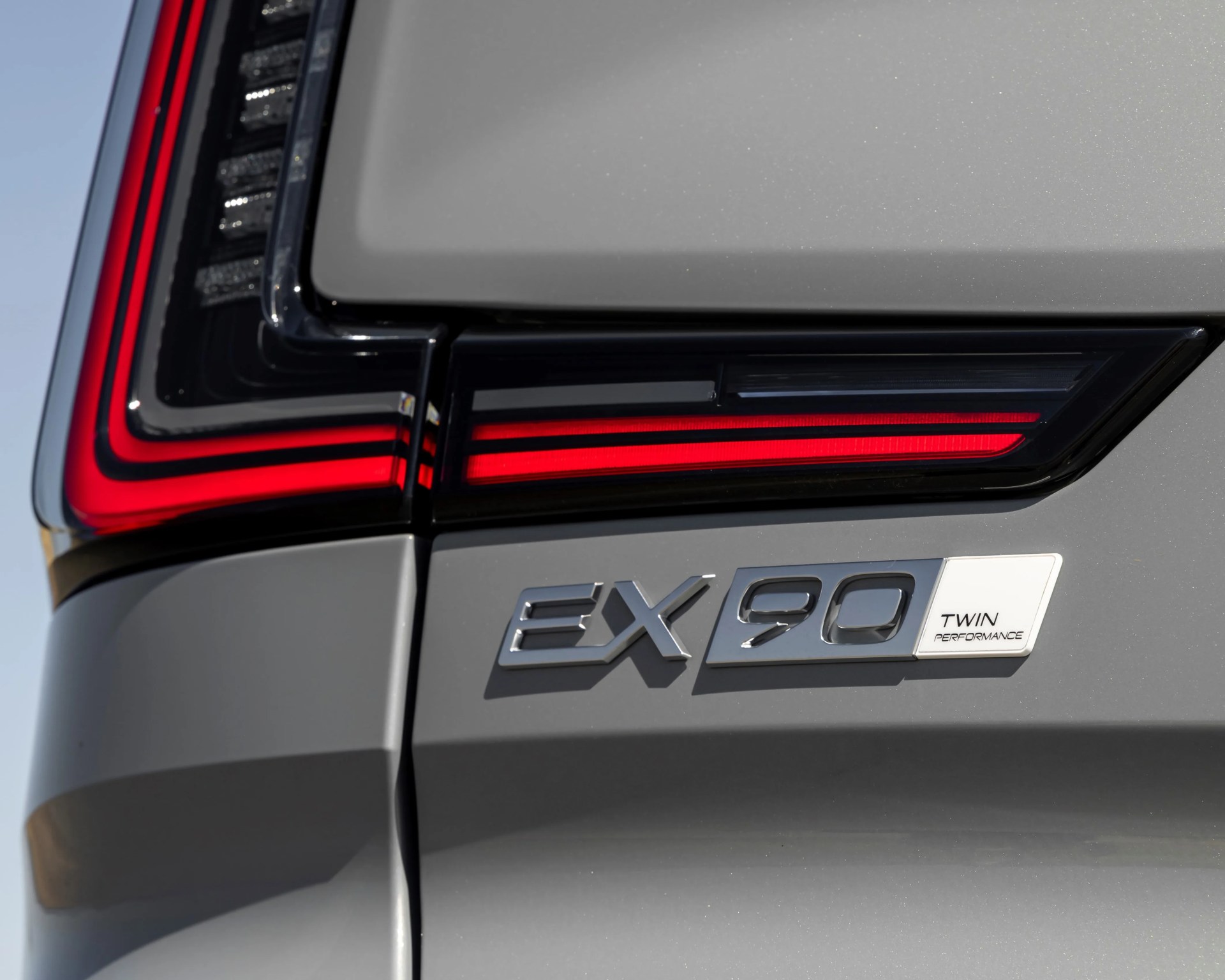 Close-up of a gray car's rear with red LED taillight and chrome "EX90 Twin Performance" badge.