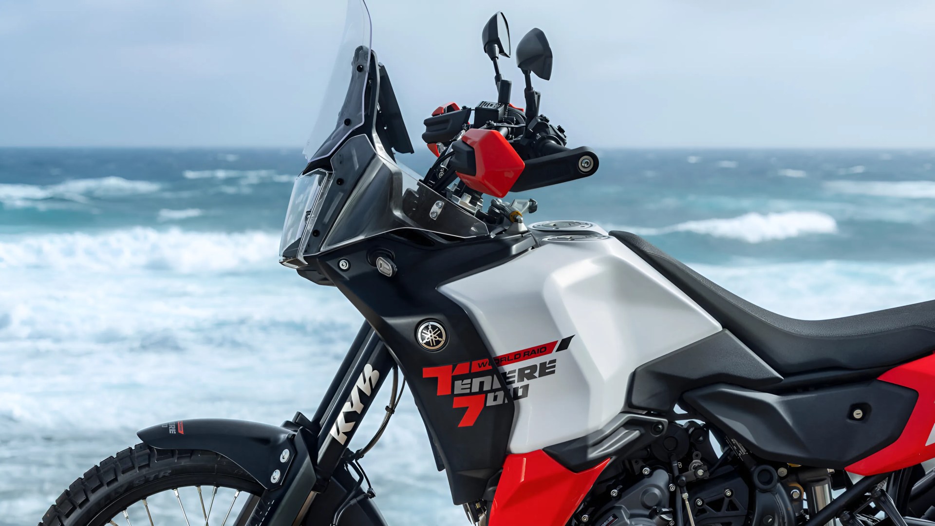 Close-up of a white and red Yamaha Tenere 700 adventure motorcycle with black accents by the ocean.