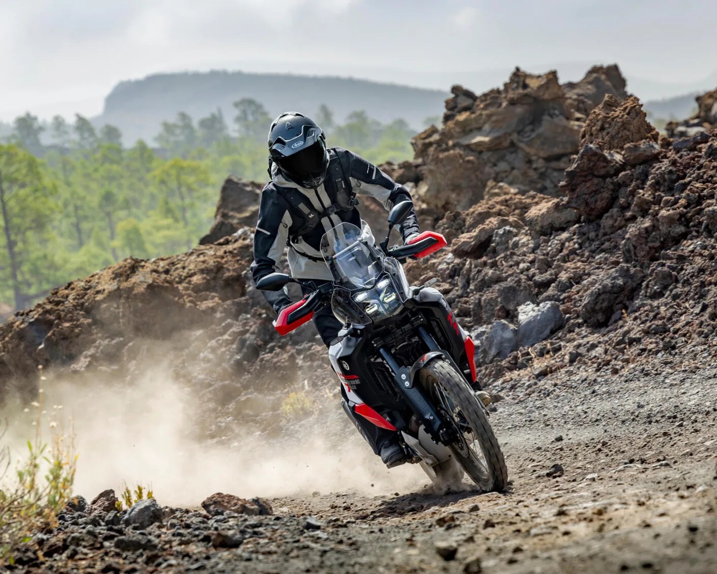 Motorcyclist wearing black and white gear riding a black and red adventure motorcycle on a rocky dirt trail.