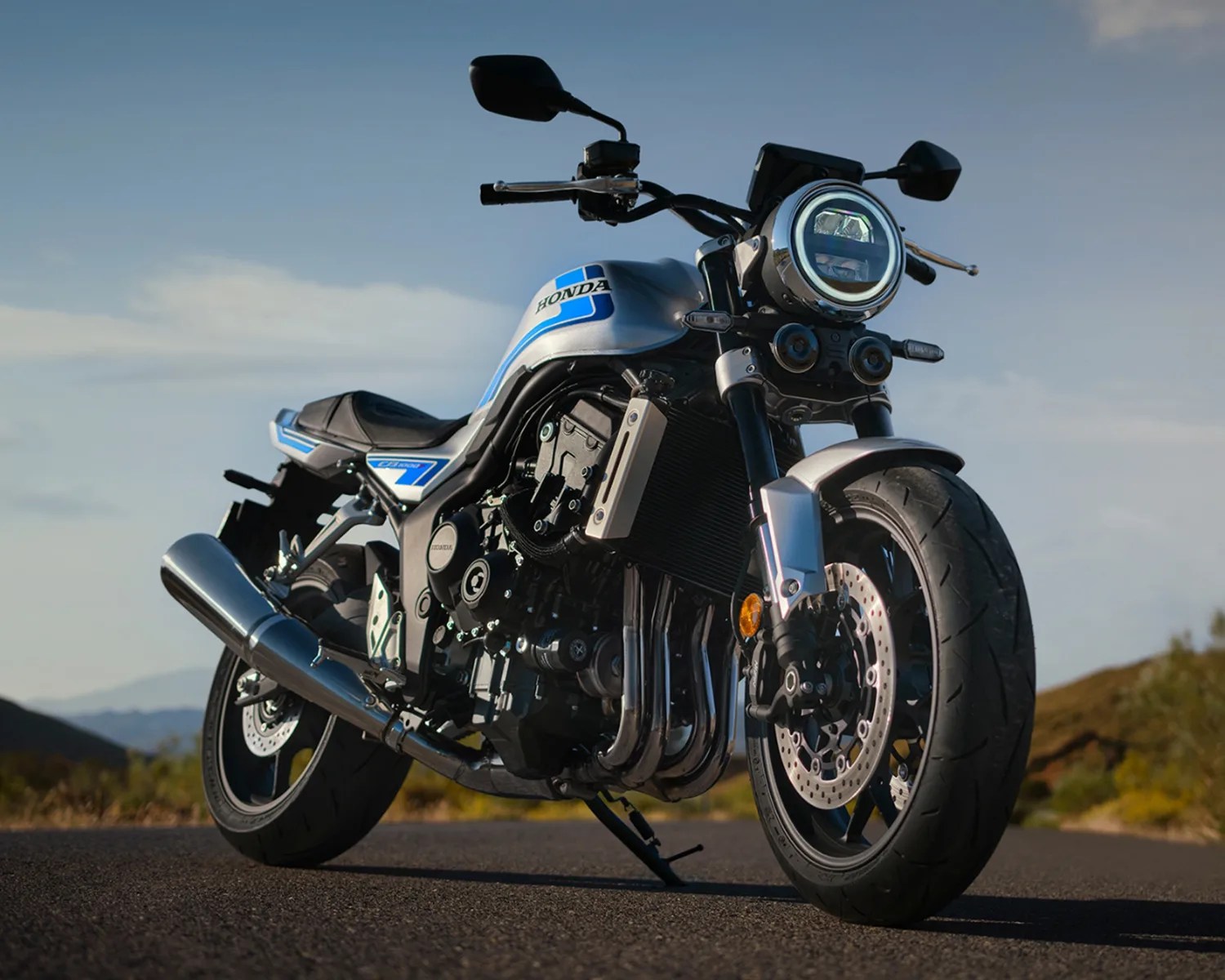 Silver and blue Honda motorcycle with round headlight parked on a road with a clear sky background.