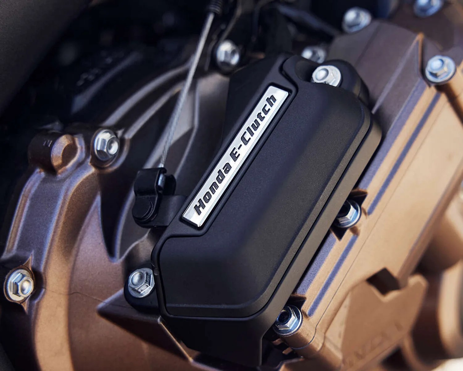 Close-up of a black Honda E-Clutch cover mounted on a bronze motorcycle engine with visible bolts.