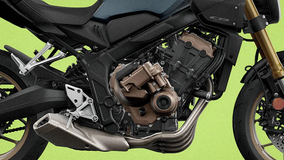Close-up of a motorcycle engine and exhaust system with black frame and gold front fork against a green background.
