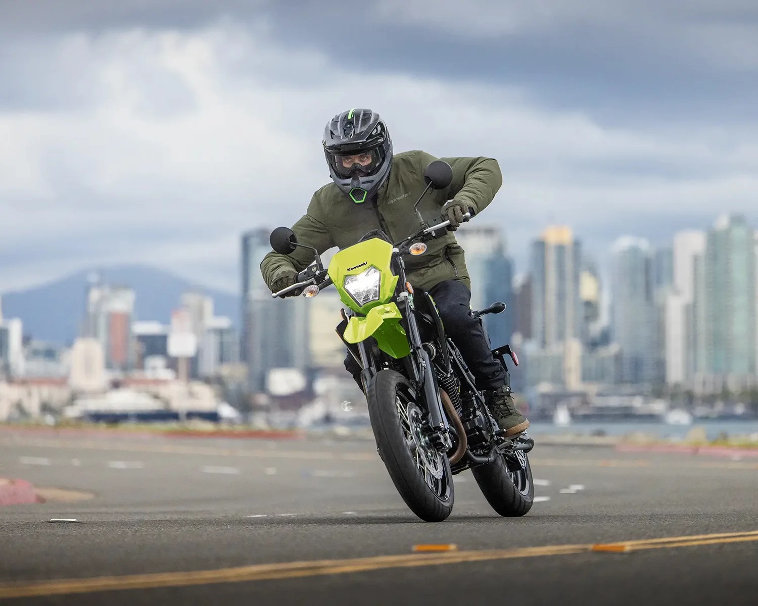 Person wearing a black helmet and green jacket riding a green Kawasaki motorcycle on a city street.