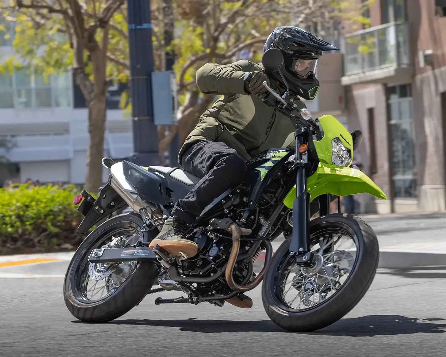 Person wearing a black helmet and green jacket riding a black and neon green Kawasaki motorcycle on a city street.