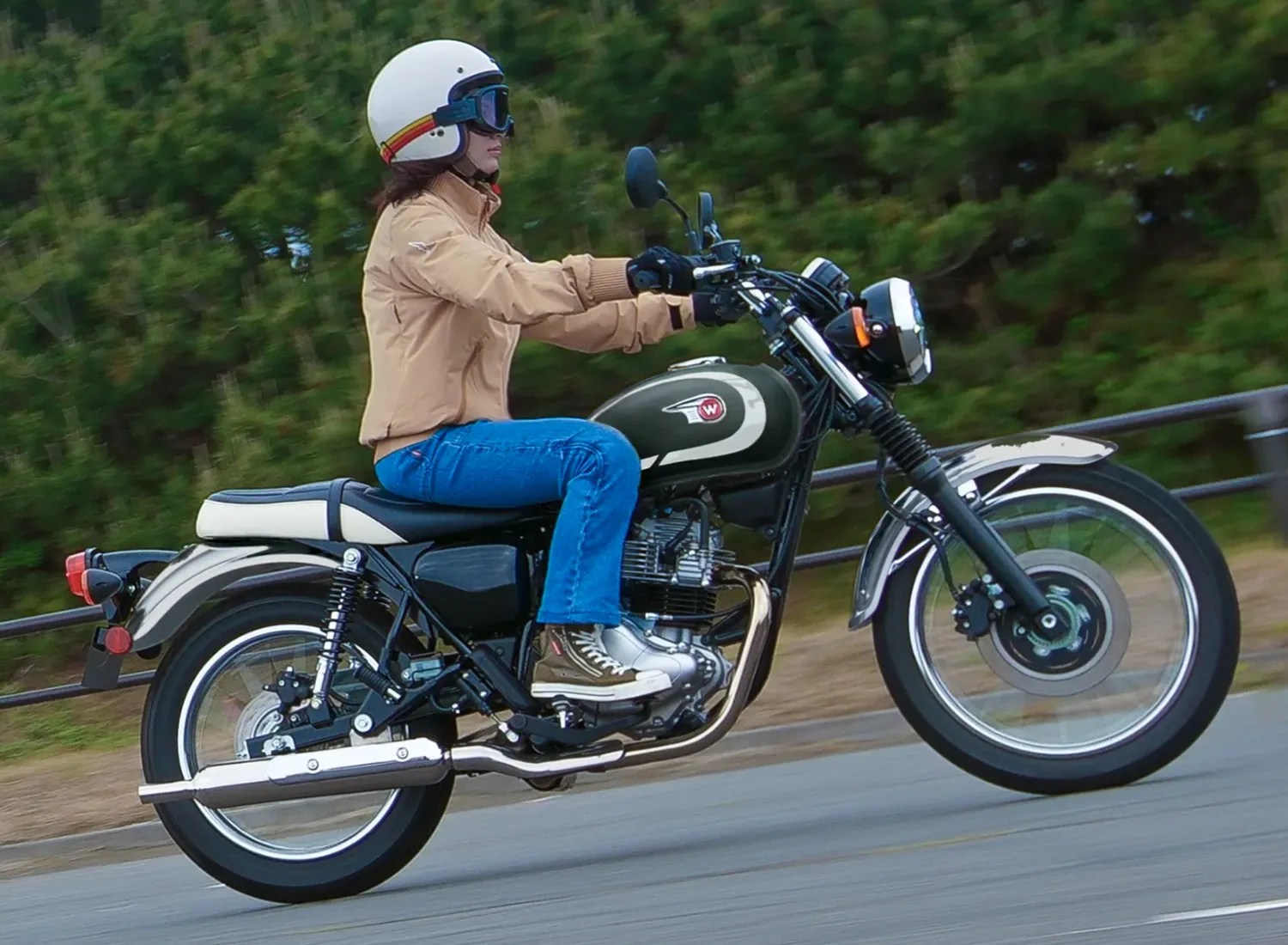 Person wearing a white helmet and beige jacket riding a green and black classic motorcycle on a road.