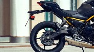 Rear section of a black motorcycle showing the rear wheel, exhaust pipe, and part of the frame with a yellow accent.