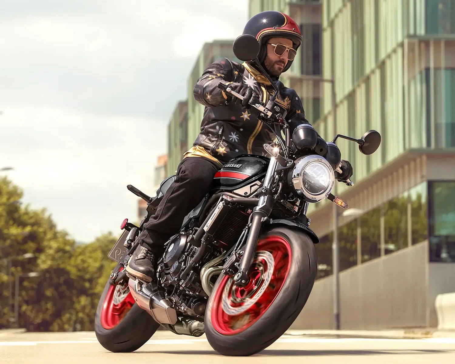 Man wearing a black star-patterned jacket and helmet riding a black Kawasaki motorcycle with red wheels on a city street.