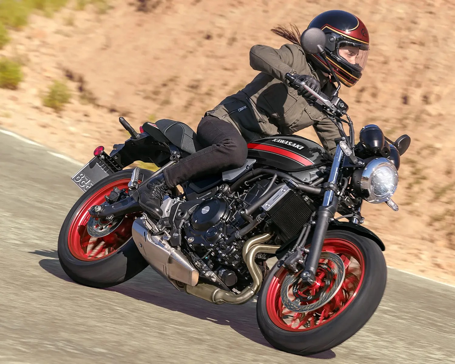 Person wearing a black and red helmet riding a black Kawasaki motorcycle with red rims on a road.