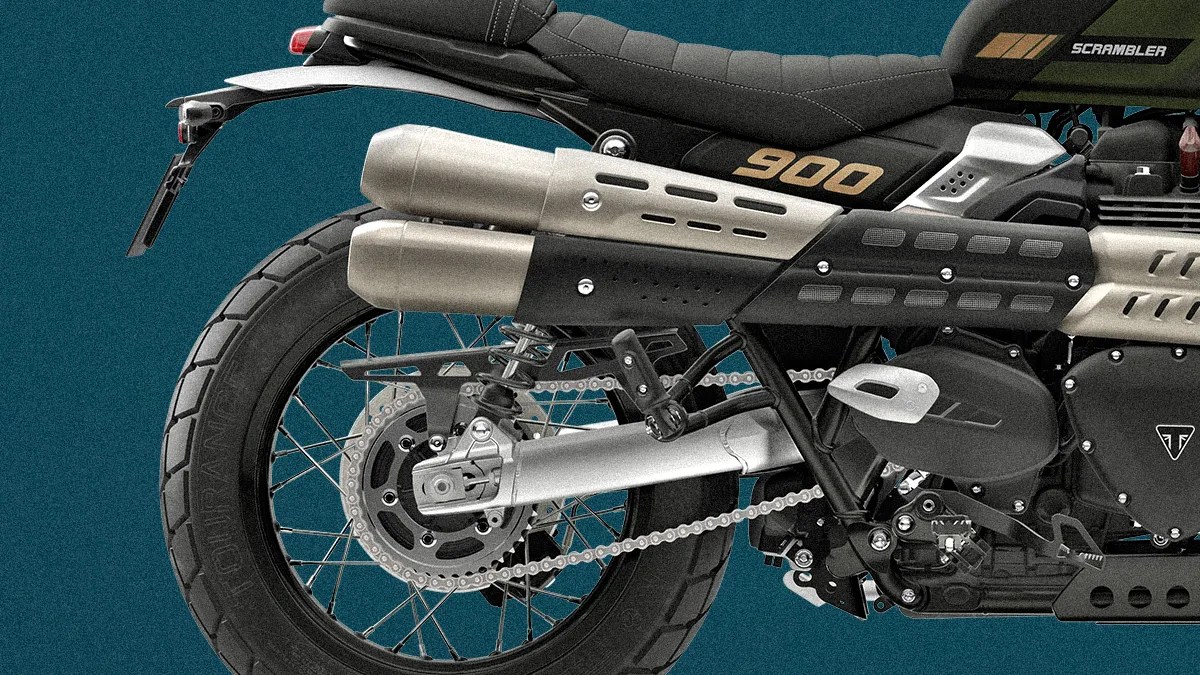 Rear section of a black and silver Triumph Scrambler 900 motorcycle showing exhaust pipes, rear wheel, and seat.