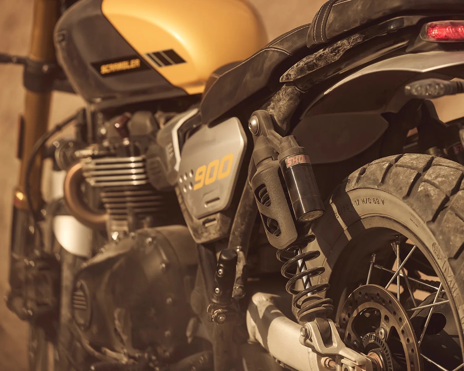 Close-up of a yellow and black Schwalbe 900 motorcycle rear suspension and tire with dirt on the parts.