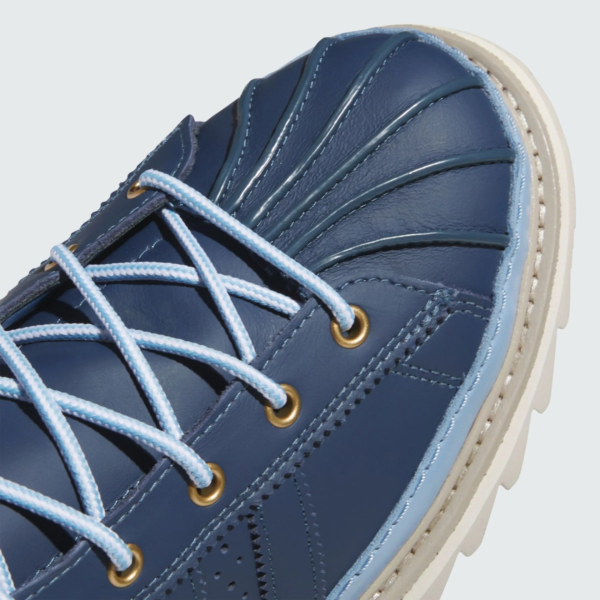 Close-up of a blue leather shoe with light blue laces, gold eyelets, and a white sole.