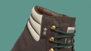 Close-up of a brown Adidas sneaker with padded white ankle collar and green laces threaded through gold eyelets.