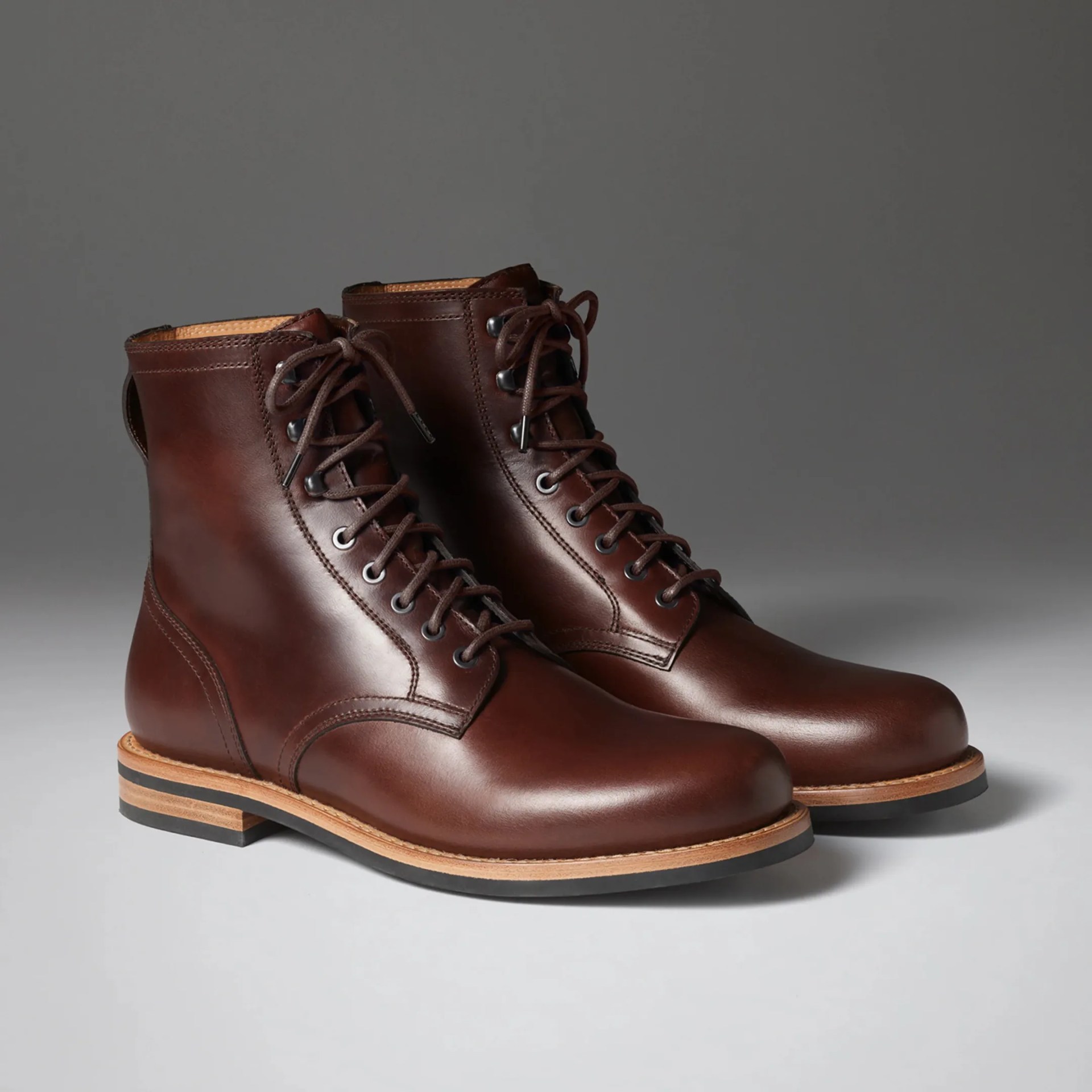 Pair of dark brown leather lace-up boots with tan midsoles and black outsoles on a gray surface.
