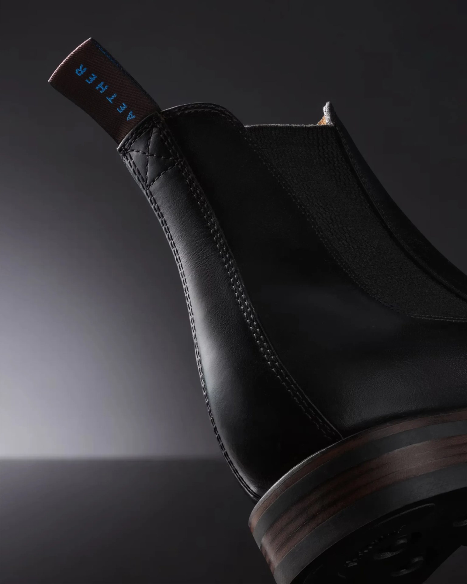 Close-up of the heel and back side of a black leather boot with a brown pull tab labeled "AETHER.